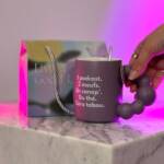 Tasse violette Femini.tea avec slogan “Zéro tabou” et coffret “Live a Good Life” sur marbre, lumière rose en fond.