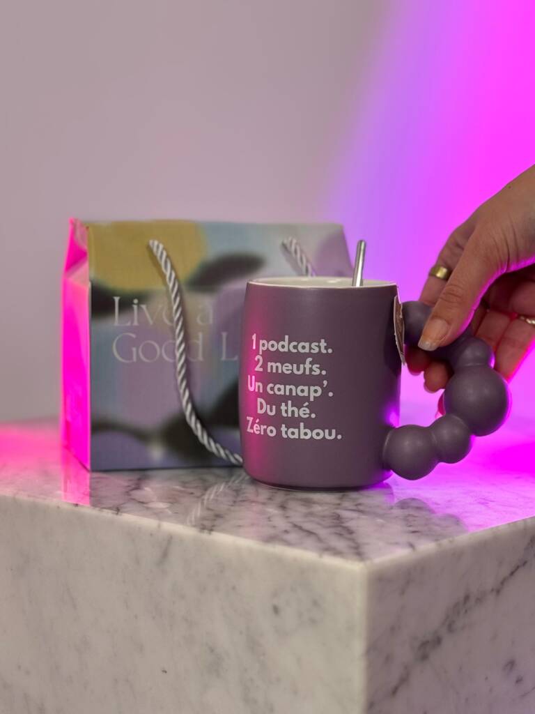 Tasse violette Femini.tea avec slogan “Zéro tabou” et coffret “Live a Good Life” sur marbre, lumière rose en fond.