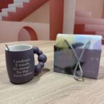 Tasse violette Chloé & Anouck by Femini.tea avec anse perlée design et cuillère, sur fond graphique rose.