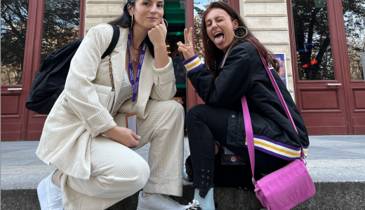 Chloé et Anouck posent devant un bâtiment, l'une en tailleur beige et l'autre avec un sac rose vif, souriantes.